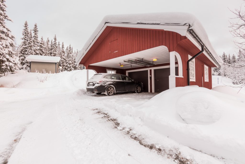 A snowy garage situated in the pine tree-dotted landscape of a New England home.
